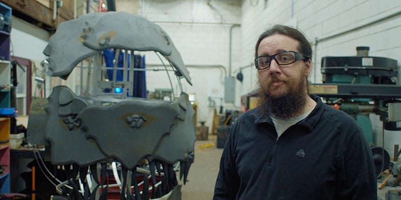 Man holding up a part in front of a screen that shows the design of the same part